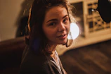 A cozy webcam setup with soft lighting highlighting a smiling woman ready to chat.