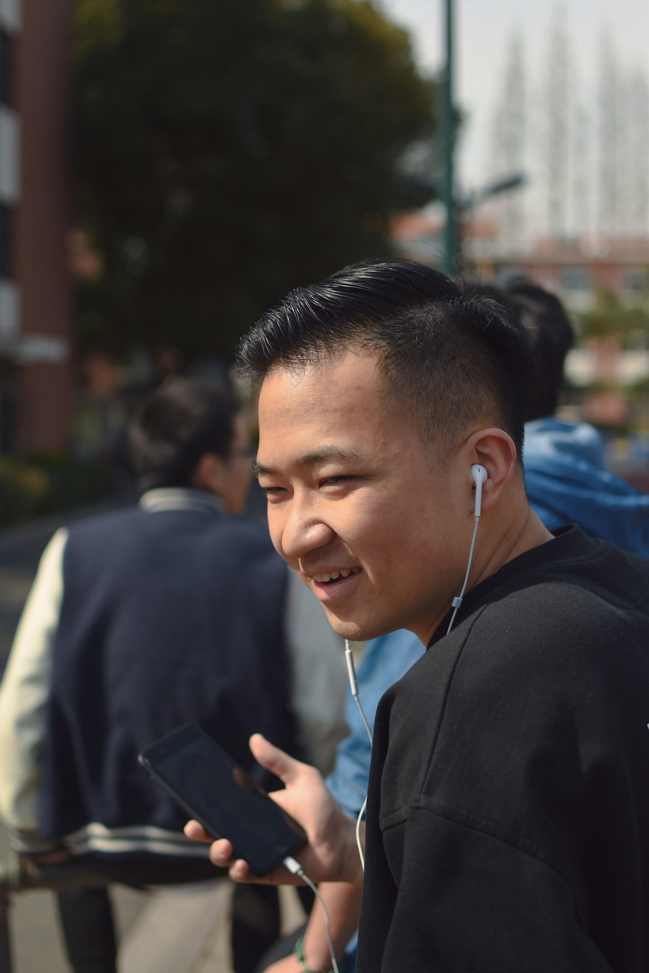 Young Latino man listening to radio on his smartphone while walking in a sunny urban park.