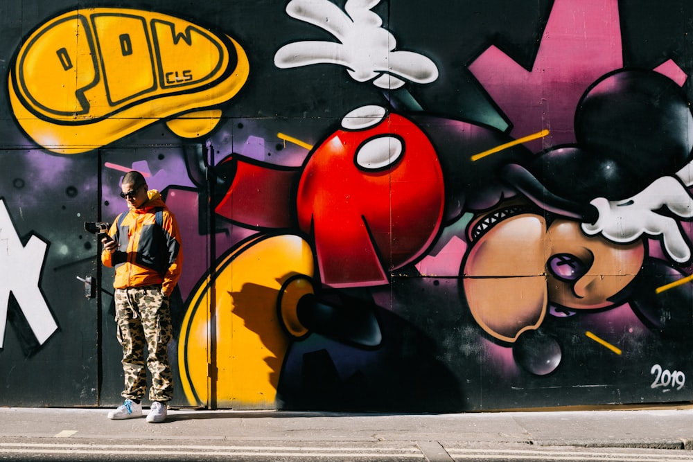 man standing beside Mickey Mouse graffiti painted wall