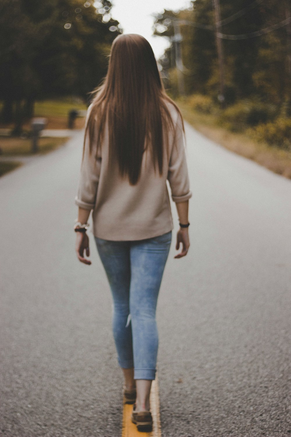 mulher na camisa cinza e calças jeans azuis andando na estrada durante o dia