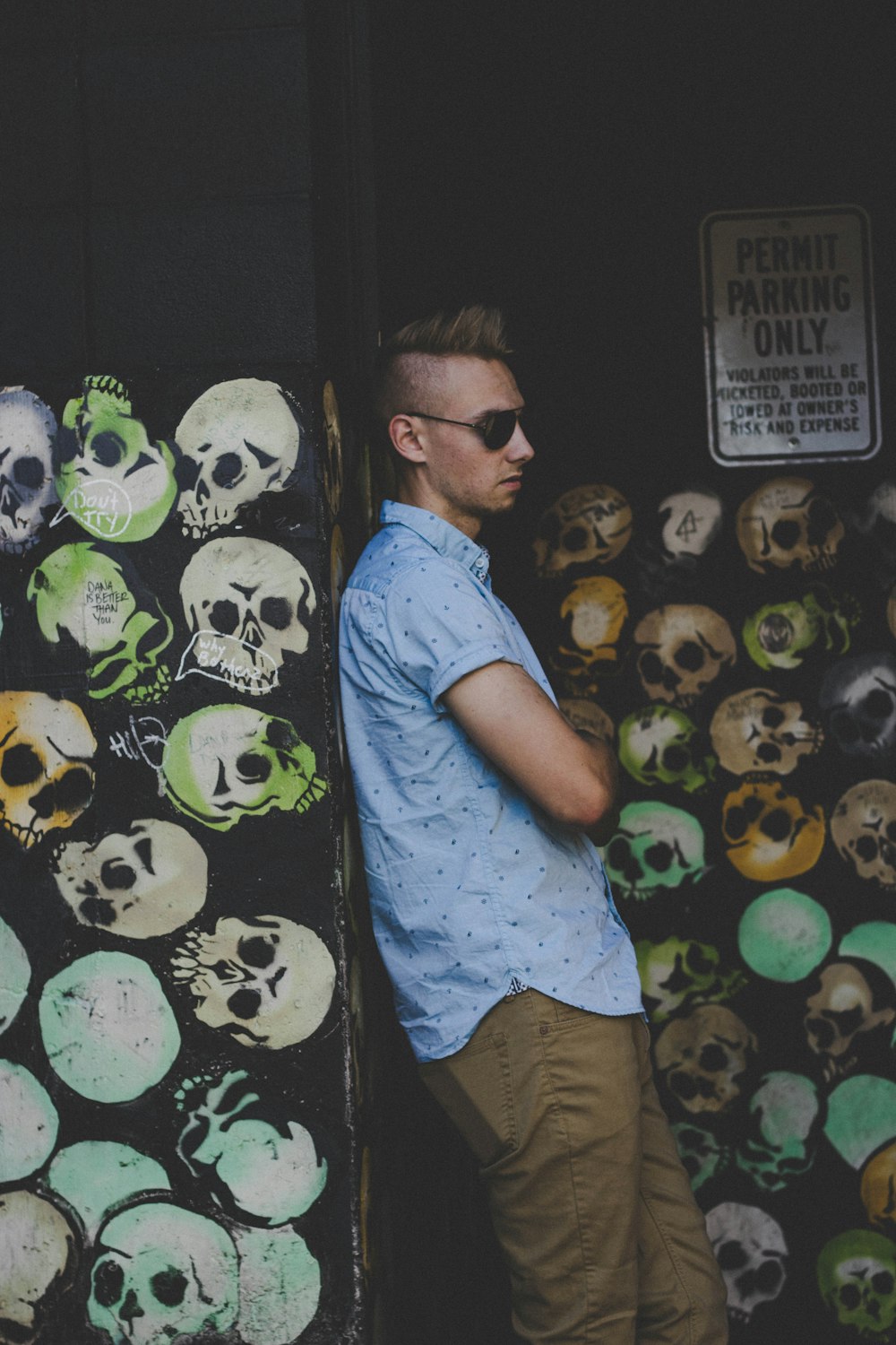 man leaning on skull painted wall wearing black sunglasses