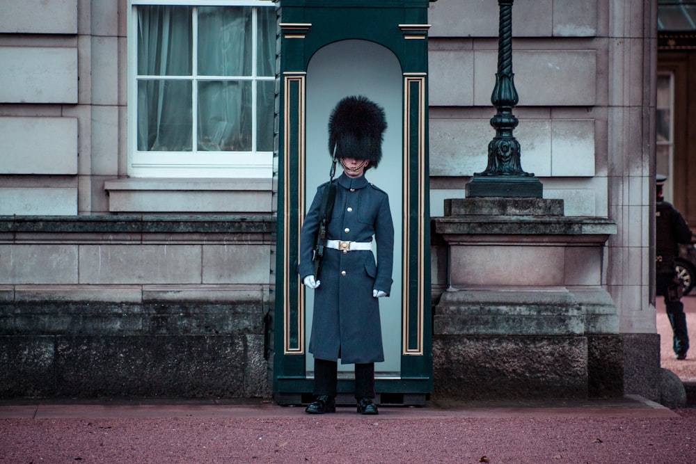 man standing beside gray house