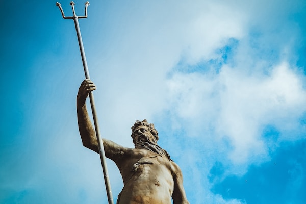 man holding trident statue under white clouds at daytime