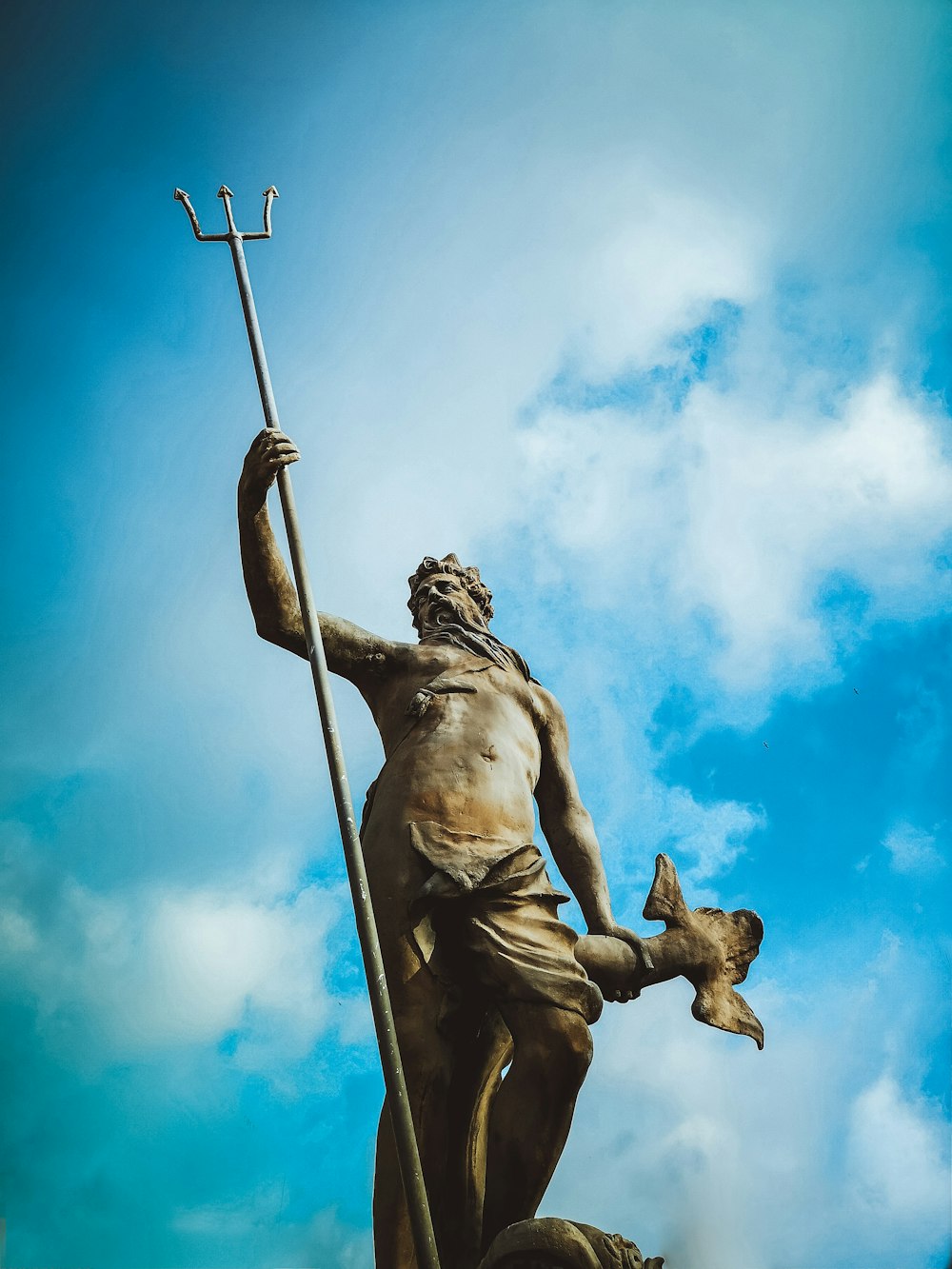 Homme tenant une statue de trident sous des nuages blancs pendant la journée