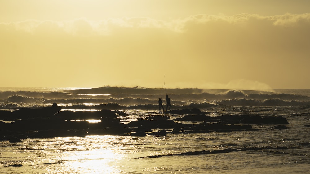 two people fishing at sea during sunset