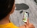 A person wearing a yellow shirt is holding a smartphone in their hand, displaying colorful app icons on the screen. The background features a grey floor with a large black silhouette of a stylized apple.