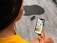 A person wearing a yellow shirt is holding a smartphone in their hand, displaying colorful app icons on the screen. The background features a grey floor with a large black silhouette of a stylized apple.