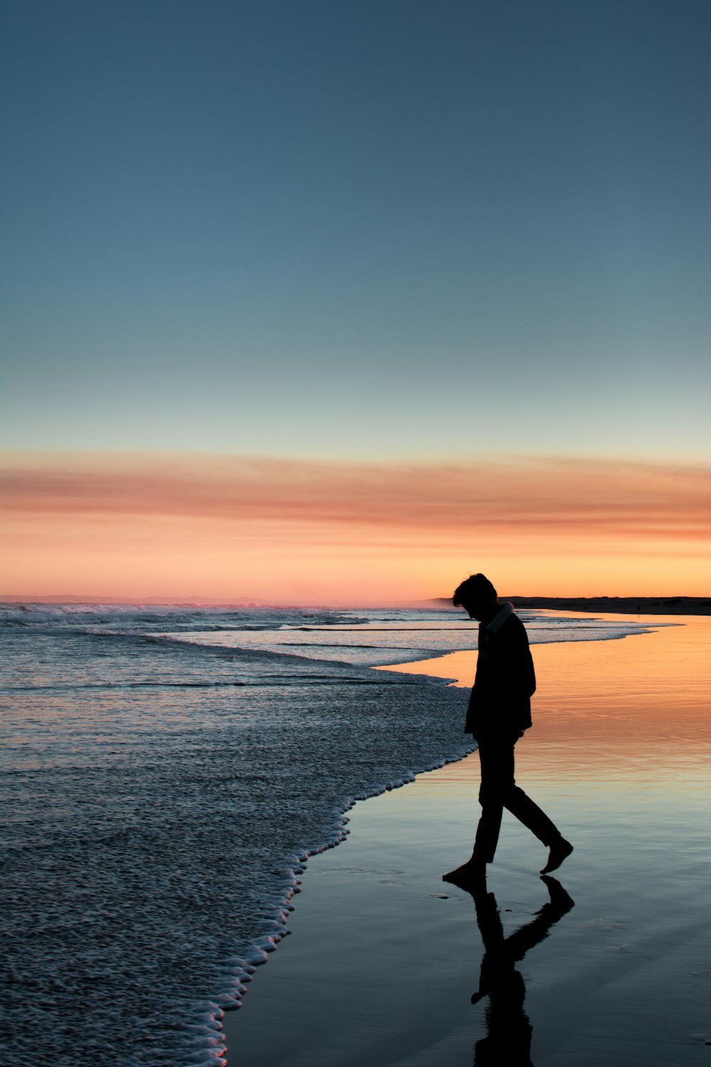 silhouette of man walking on seashore under orange sky