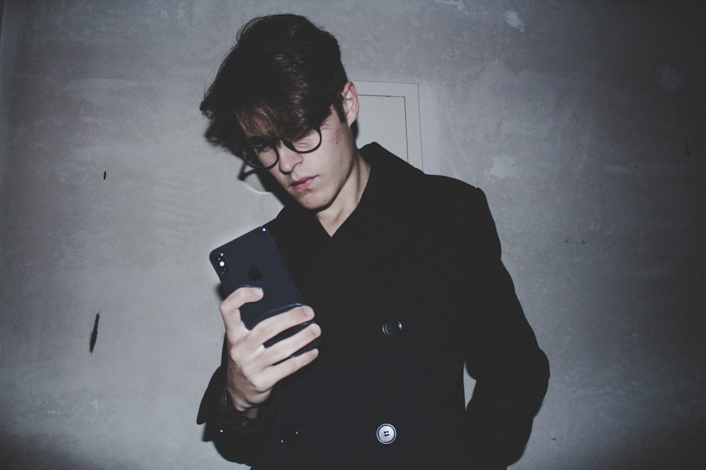 man wearing black jacket while holding iPhone X