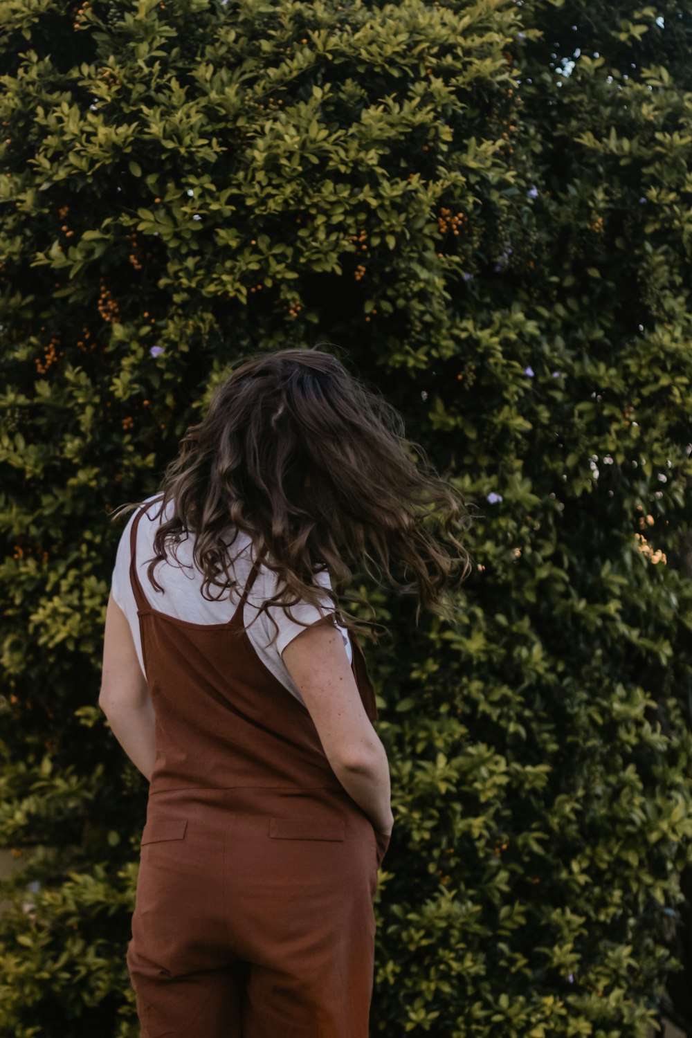 woman wearing white t-shirt and brown tank overalls near bush during daytime