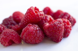 Close-up of ripe red raspberries glistening with morning dew on a green bush.