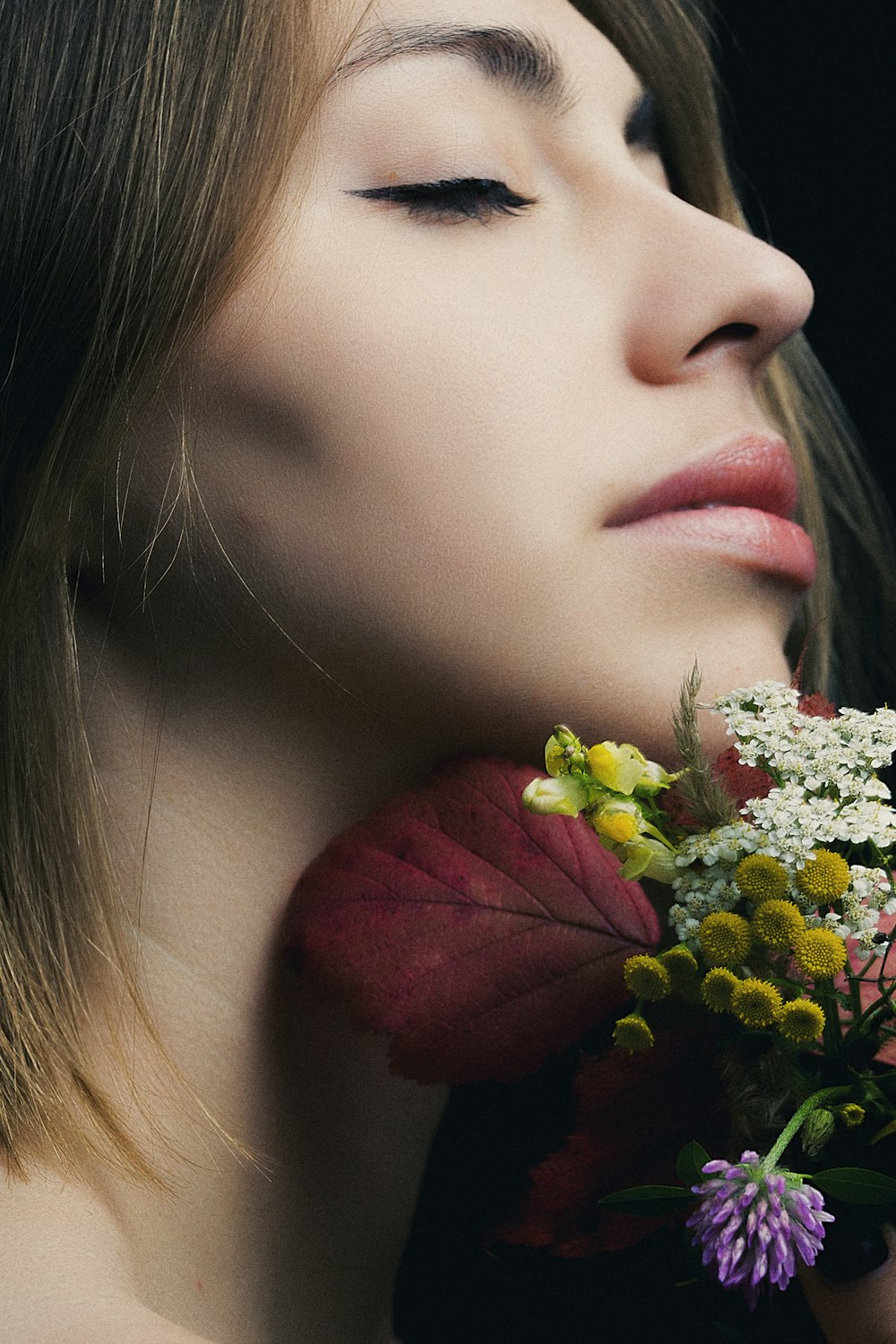 woman closing her eyes next to flowers