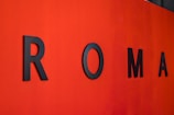 Large black letters spelling out 'ROMA' are mounted on a vibrant red wall.