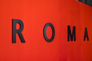 Large black letters spelling out 'ROMA' are mounted on a vibrant red wall.