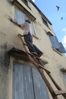 A craftsman painting wooden shutters with UV-resistant lasure on a sunny day.