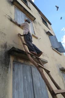 A craftsman painting wooden shutters with UV-resistant lasure on a sunny day.