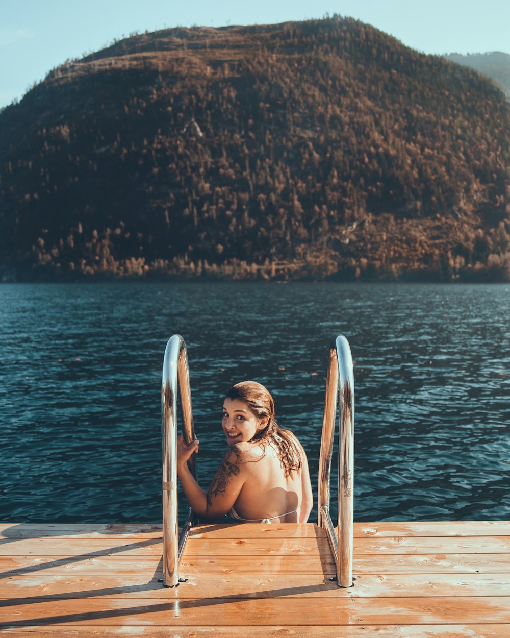 mulher usando sutiã branco sentado em escadas perto do corpo de água