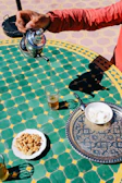 Traditional Moroccan tea being poured in an ornate silver teapot into small glasses on a patterned tray.