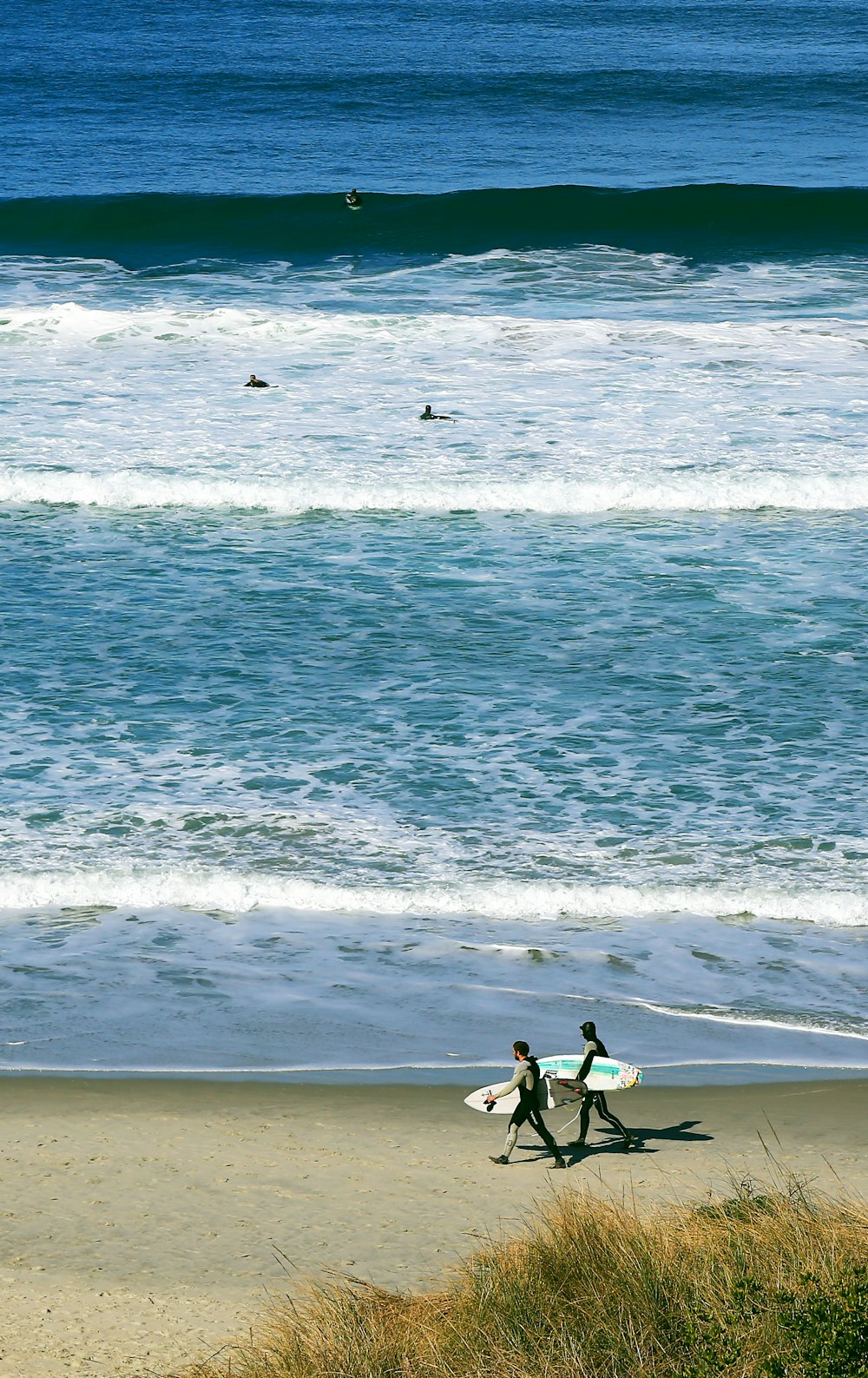 Dos personas caminando por la orilla del mar mientras sostienen tablas de surf