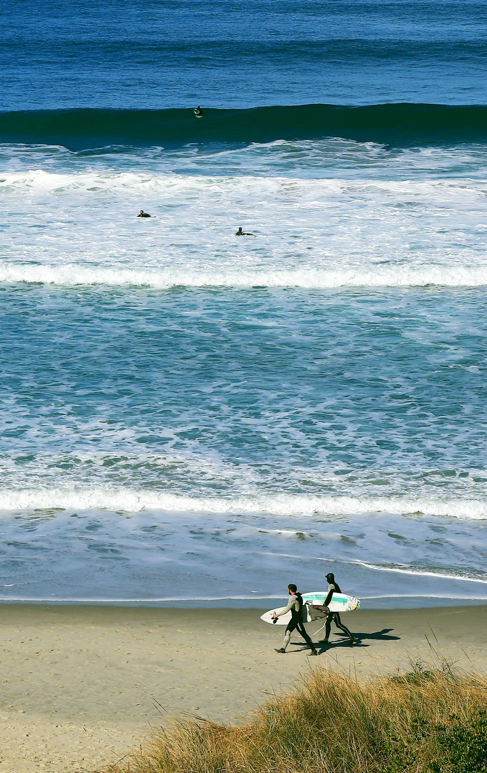 zwei Personen, die am Meeresufer spazieren gehen, während sie Surfbretter halten