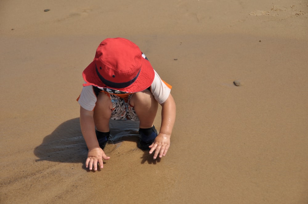 child wearing red hat touching sand