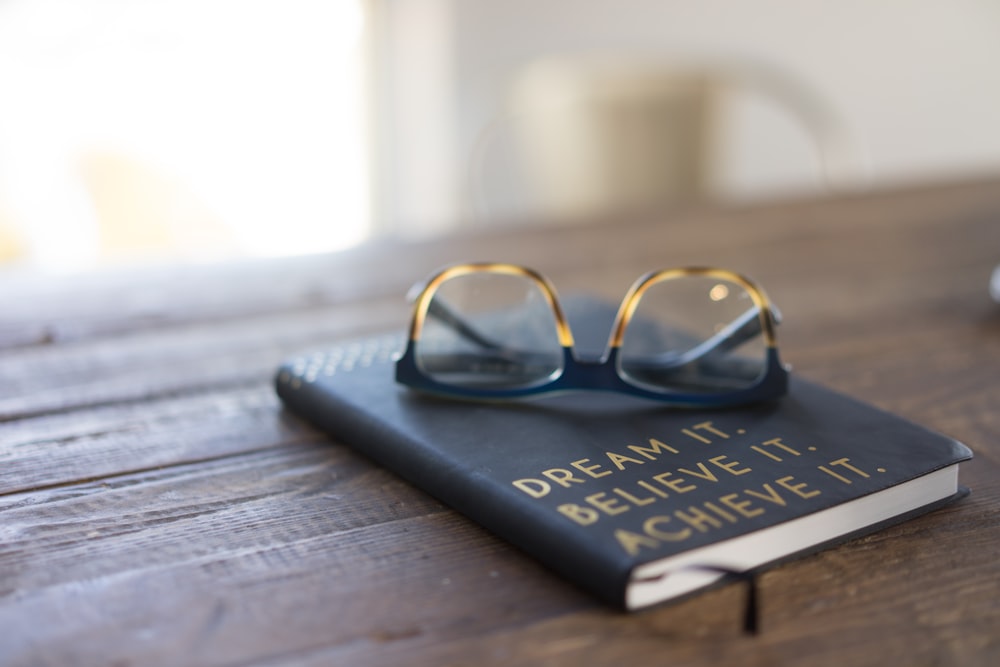 Schwarze und braune Brille auf Buch auf braunem Holztisch