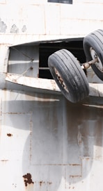 A pair of large, industrial tires are mounted on a rusted metal surface, possibly part of an old airplane or industrial vehicle. The surface is weathered with rust spots and peeling paint, suggesting age and disuse.