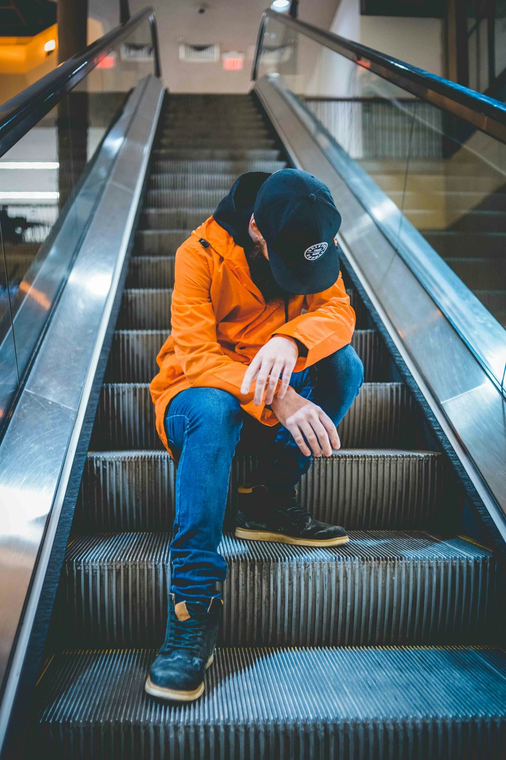 man in brown jacket and blue pants sitting on escalator