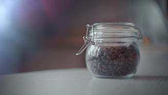 An elegant glass jar filled with rare coffee beans, softly illuminated against a dark backdrop.