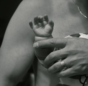 Top view of a parent’s hand gently holding a baby’s hand next to a smart wearable baby device