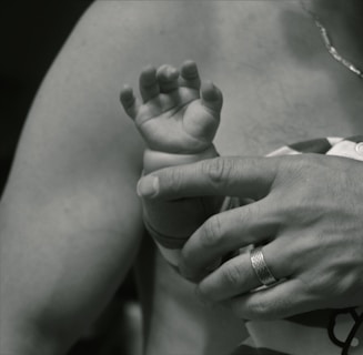 Top view of a parent’s hand gently holding a baby’s hand next to a smart wearable baby device