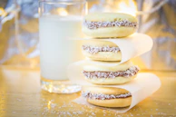 Artisan alfajores stacked on a cream-colored plate with a drizzle of dulce de leche.