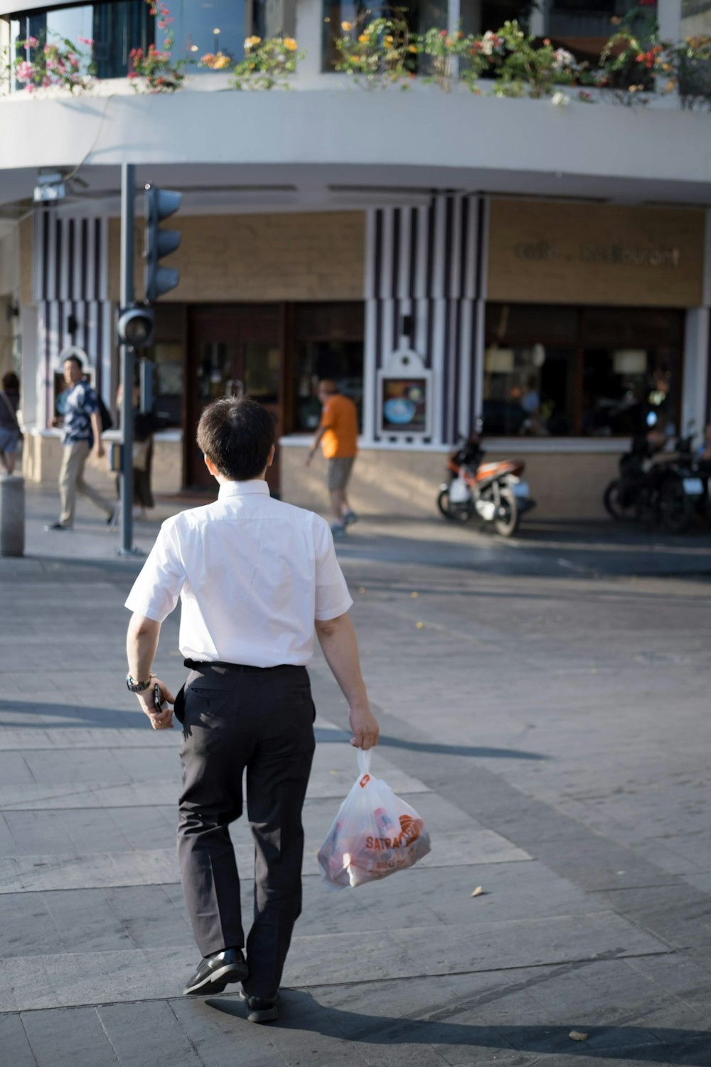 man holding plastic bag while walking at middle of street