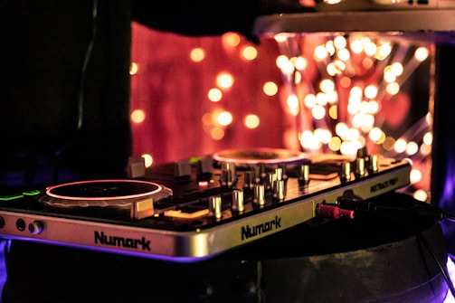 A DJ controller is prominently displayed with illuminated turntables and control knobs, set against a backdrop of vibrant bokeh lights, creating a festive and dynamic atmosphere.