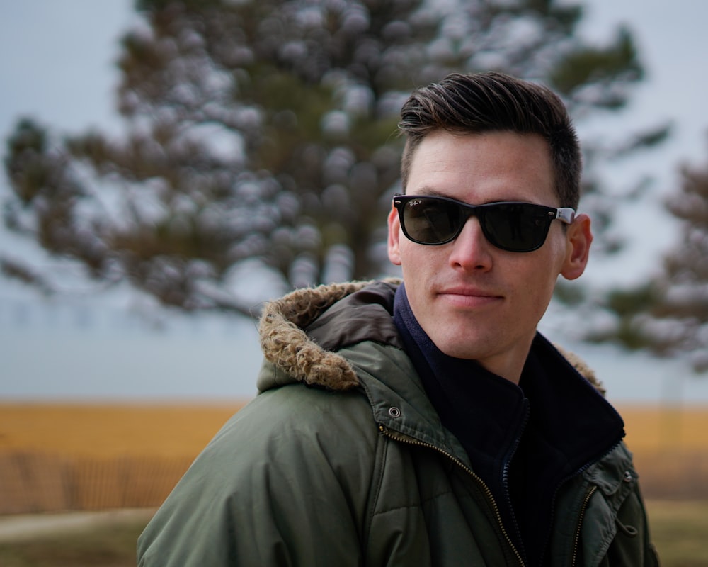 a man in a parka and sunglasses standing in front of a tree