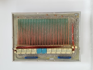 A vintage electronic circuit board featuring an array of vertical red and green wires. The board is rectangular with various components including resistors and connectors. Its design and components suggest it might be from an early computer or electronic device.