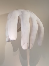 A large, sculpted white hand is hanging vertically, resembling a life-like human hand. The fingers are slightly curved, and the detail in the contours and shading gives it a realistic appearance.