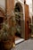 An ornate doorway framed by intricate wooden carvings and detailed mosaic tiles. The scene includes a potted plant with long, thin leaves and a traditional Moroccan lantern placed on a geometric patterned tile floor.
