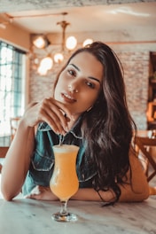 smiling woman sitting near table holding straw