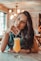 smiling woman sitting near table holding straw