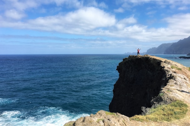 A joyful traveler standing on a cliff overlooking a vibrant sunrise above miles of ocean.