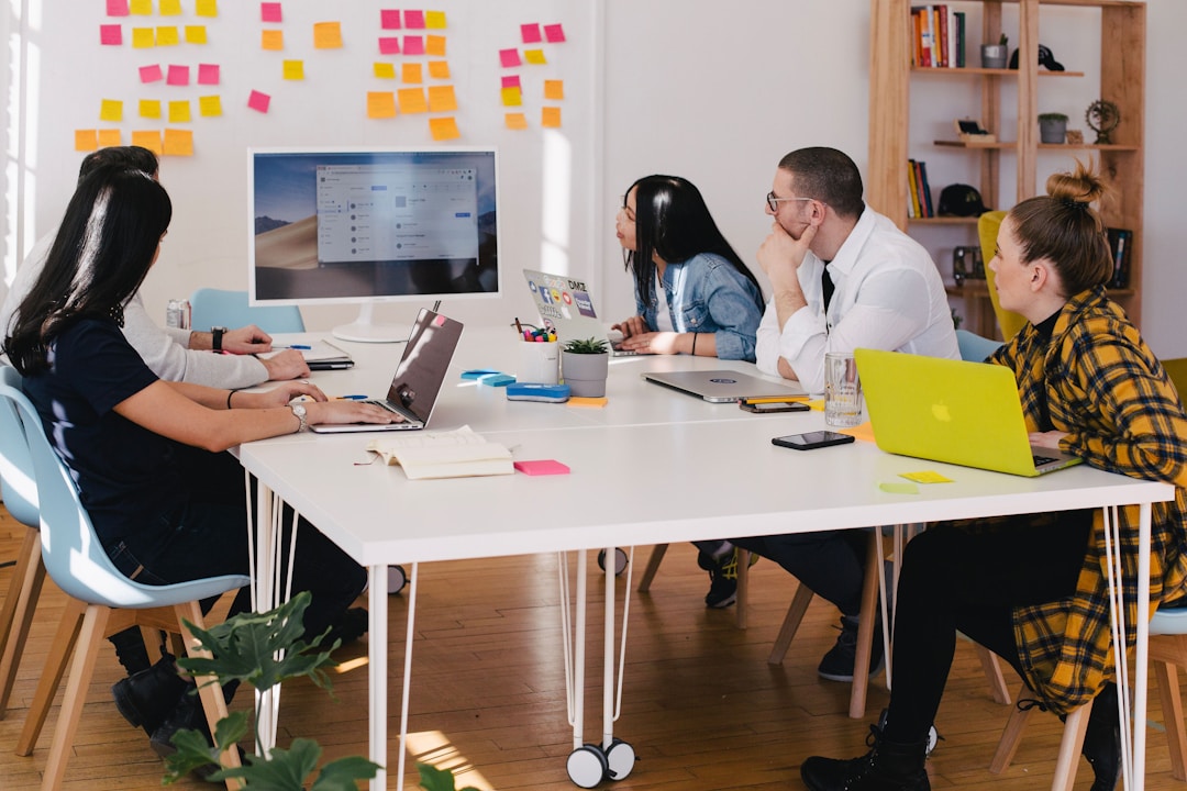 A team sitting at a white table with laptops looking at a computer screen discussing the benefits of performance analytics.