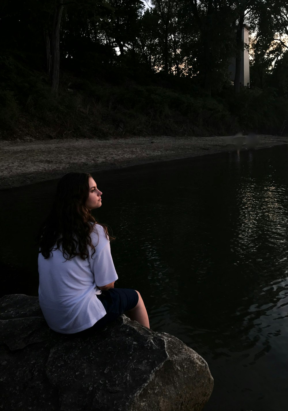 woman sitting on rock while facing lake