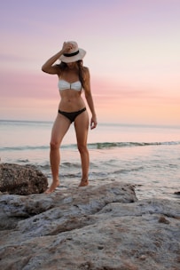 woman in black and white bikini standing on rock formation near sea during golden hour