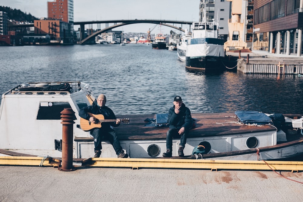men sitting while playing guitar on boat at dock during daytime