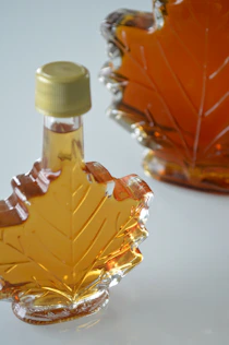 Golden maple syrup dripping from a wooden tap into a glass jar on a rustic farm table.