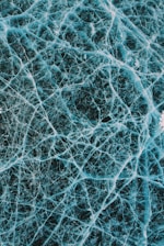 A detailed network of intricate cracks spreads across a surface, resembling cracked ice or glass. The patterns are irregular, forming a complex web of lines in varying thickness.