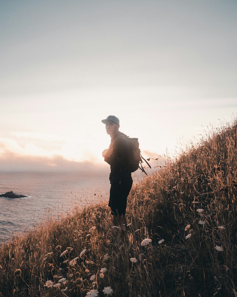 man with backpack standing at the hill overlooking the ocean