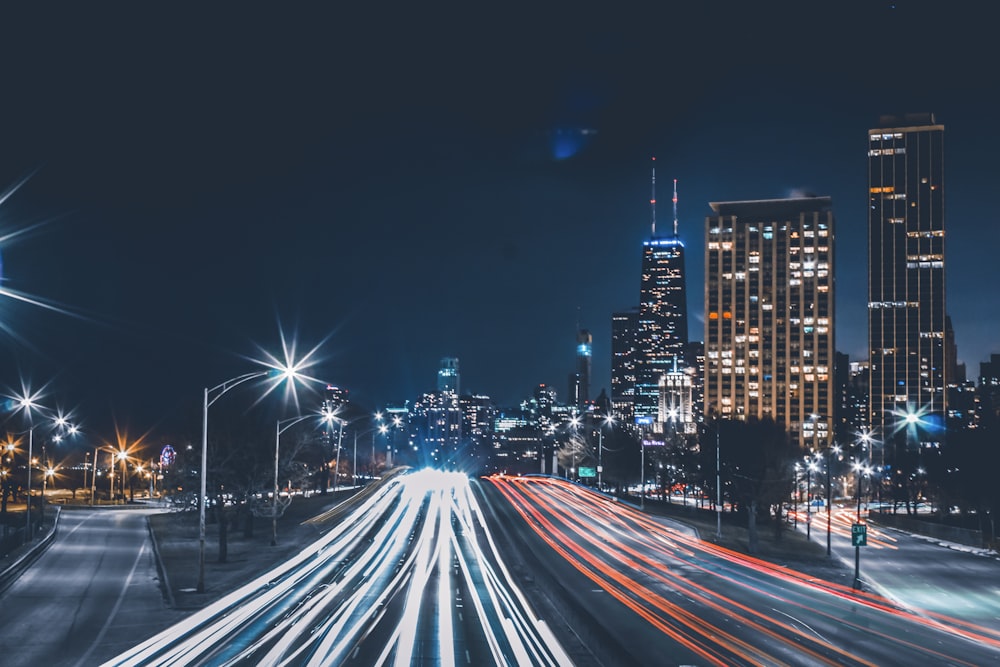 Fotografía timelapse de luces traseras de vehículos en carretera con edificios de gran altura