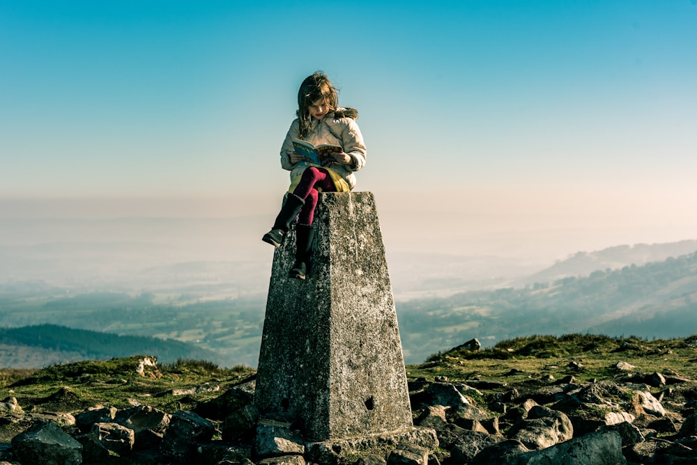 a woman sitting on top of a stone pillar